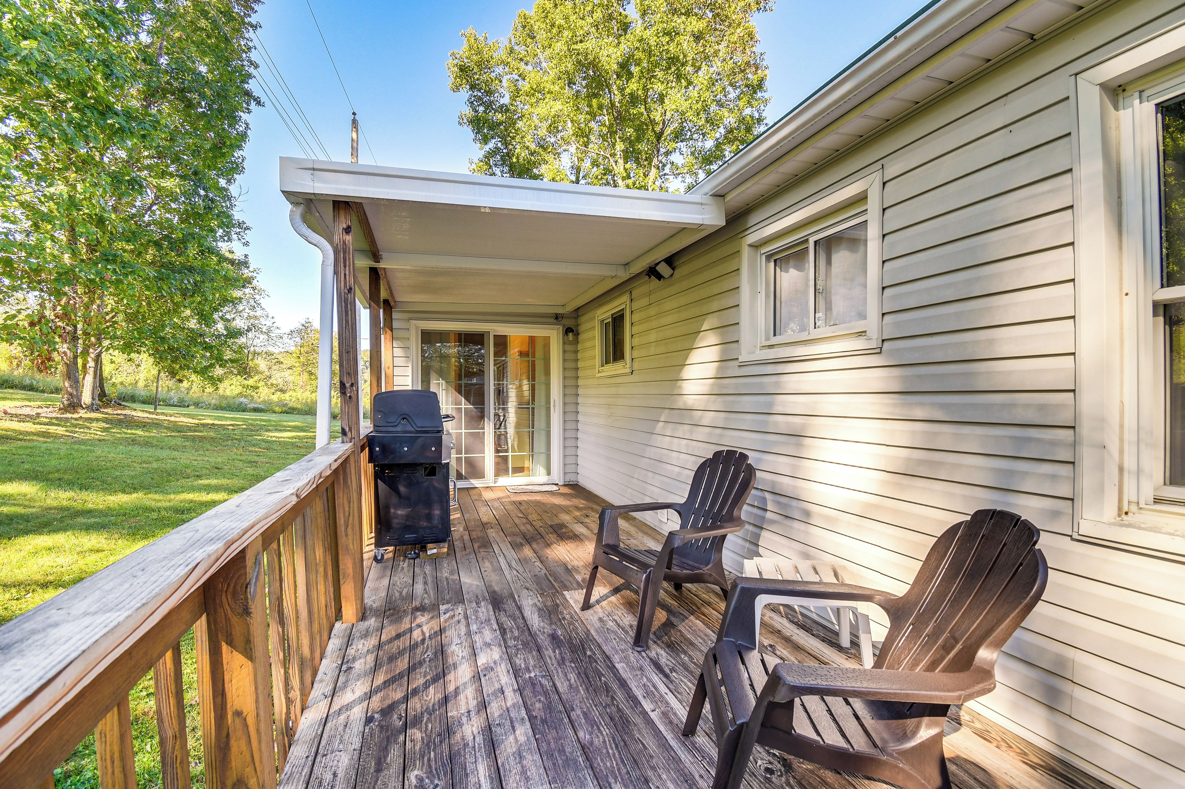 A covered porch with a grill, two Adirondack chairs, and a wooden deck.