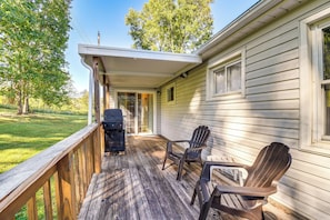 Eine überdachte Veranda mit Grill, zwei Adirondack-Stühlen und einer Holzterrasse.