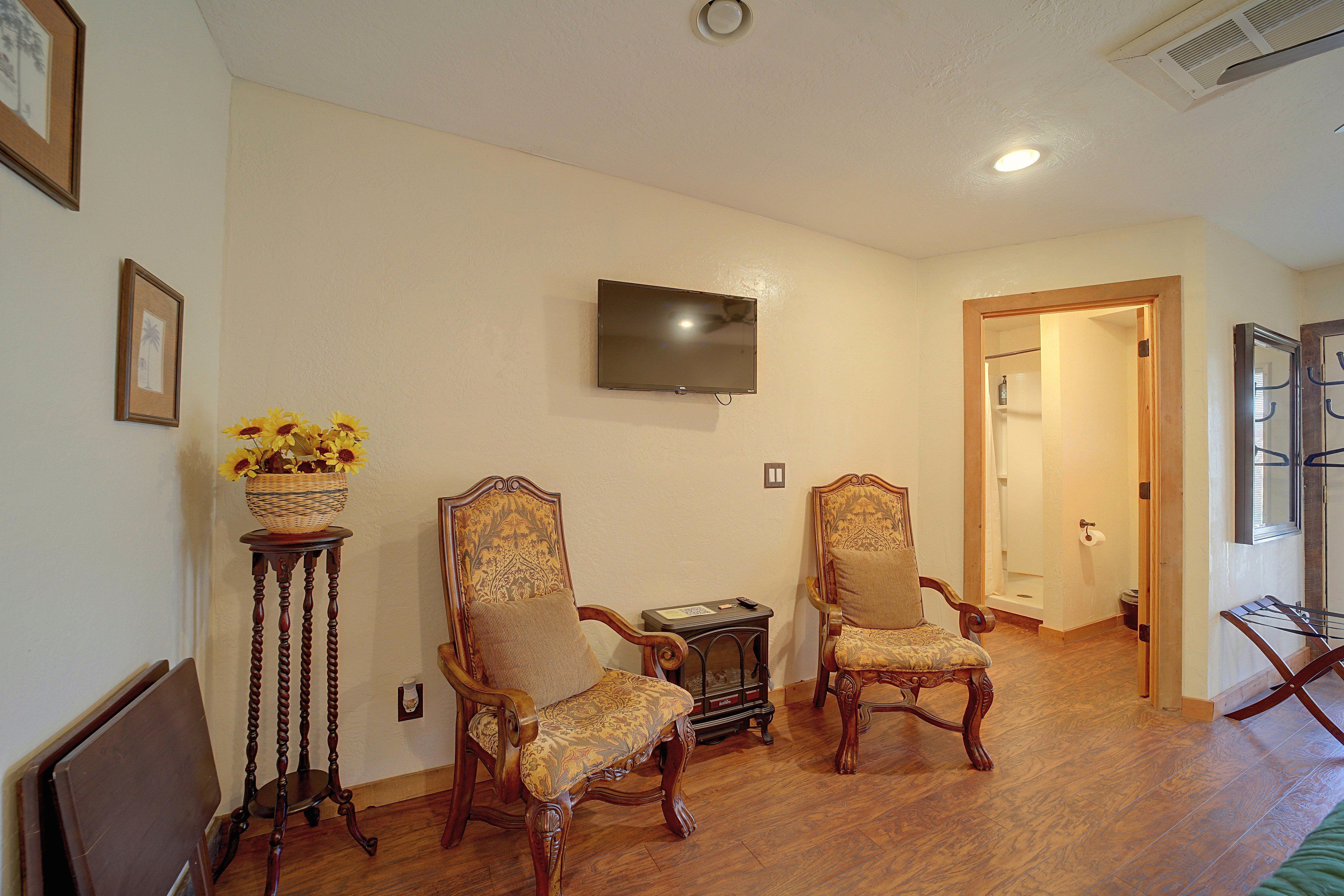 A room with two ornate chairs, a television on the wall, and a wooden floor.