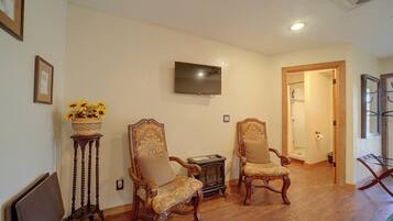 A room with two ornate chairs, a television on the wall, and a wooden floor.