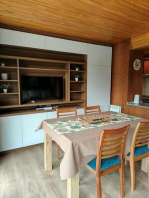 Een eethoek met een houten tafel, stoelen en een aan de muur bevestigde televisie.