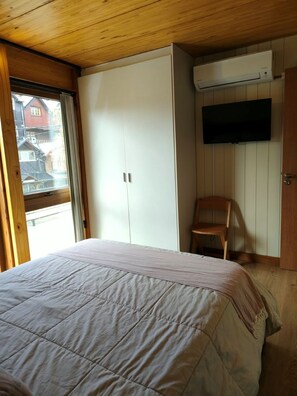Een slaapkamer met een bed, een kledingkast, een stoel en een televisie aan de muur.