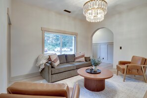 A modern living room with a sofa, armchairs, a coffee table, and a large window with a view of trees and parked cars.