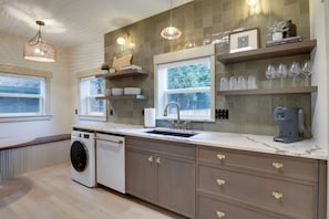 A modern kitchen with a built-in washing machine, a coffee machine, and a window with a view of trees.