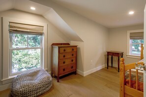 Quarto com teto inclinado, cômoda de madeira, mesa pequena, poltrona de saco e berço.