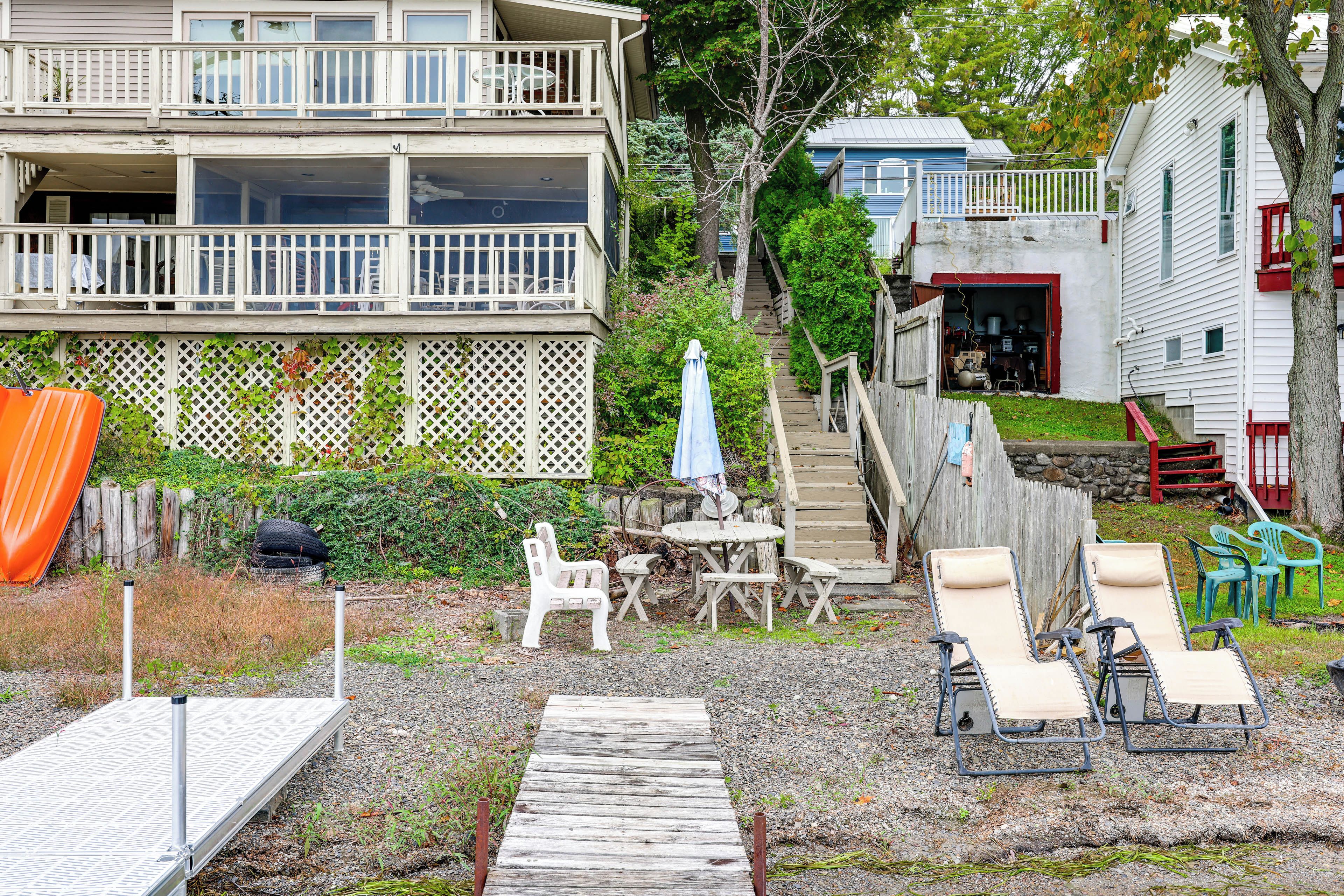 A residential property with a two-story building, a wooden deck, outdoor furniture, and a staircase leading to a garage.
