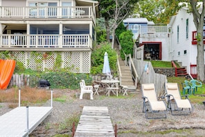 A residential property with a two-story building, a wooden deck, outdoor furniture, and a staircase leading to a garage.