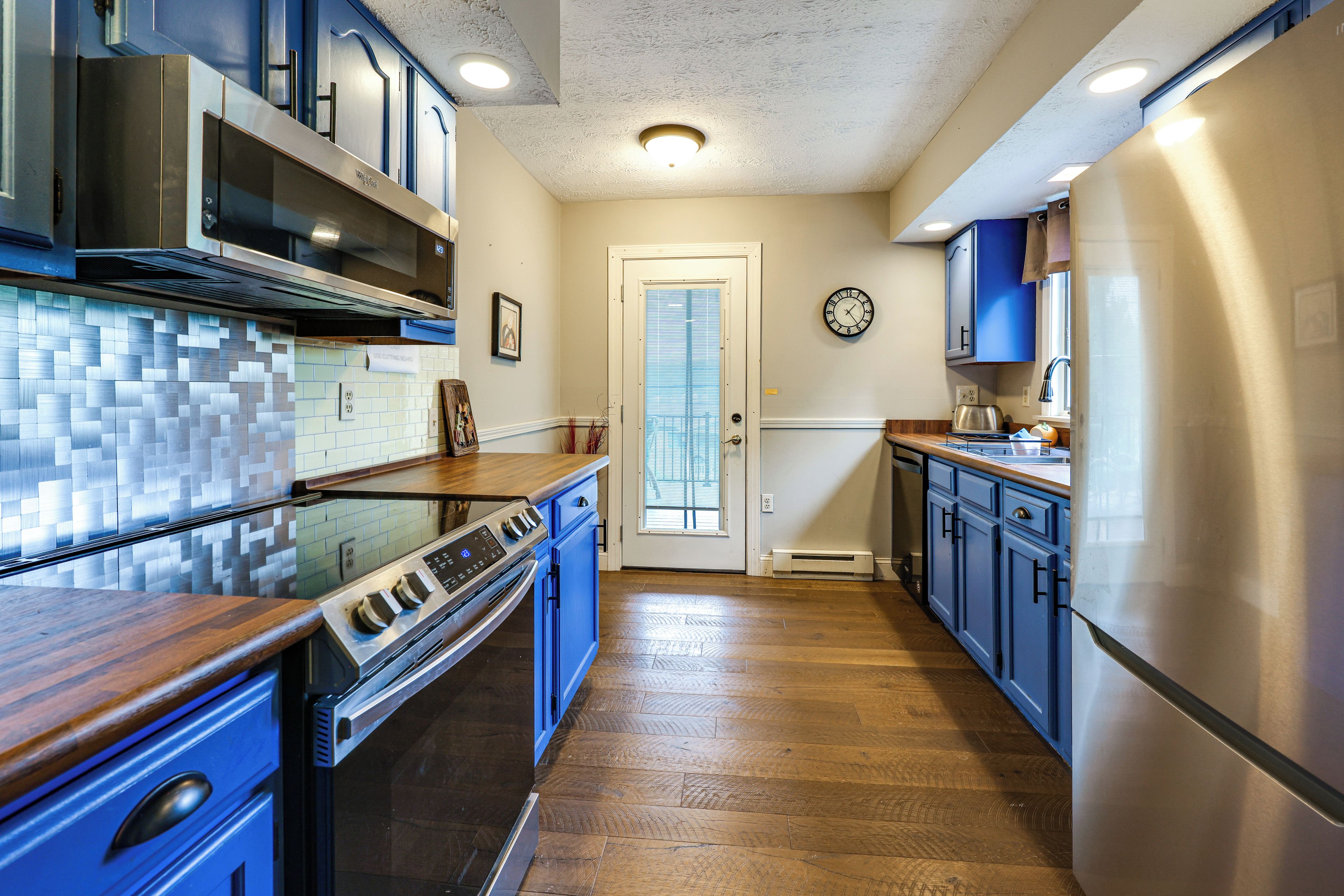 A kitchen with a tiled backsplash, stainless steel appliances, and wooden flooring.