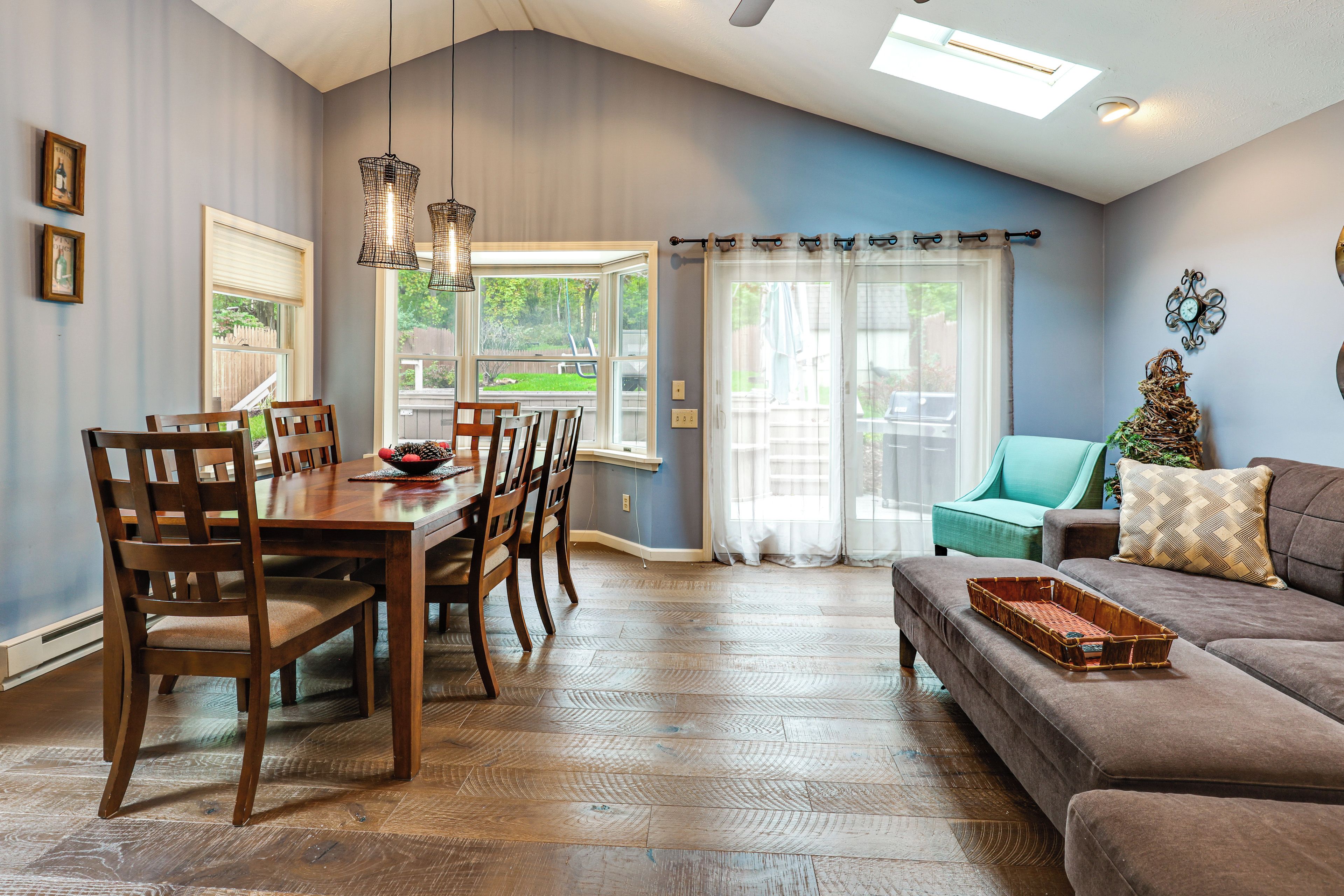A dining area with a wooden table and chairs, a living room with a sofa and a window, and a ceiling with a skylight.