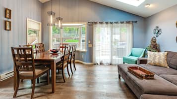 A dining area with a wooden table and chairs, a living room with a sofa and a window, and a ceiling with a skylight.