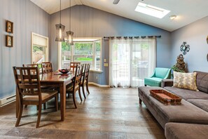 A dining area with a wooden table and chairs, a living room with a sofa and a window, and a ceiling with a skylight.