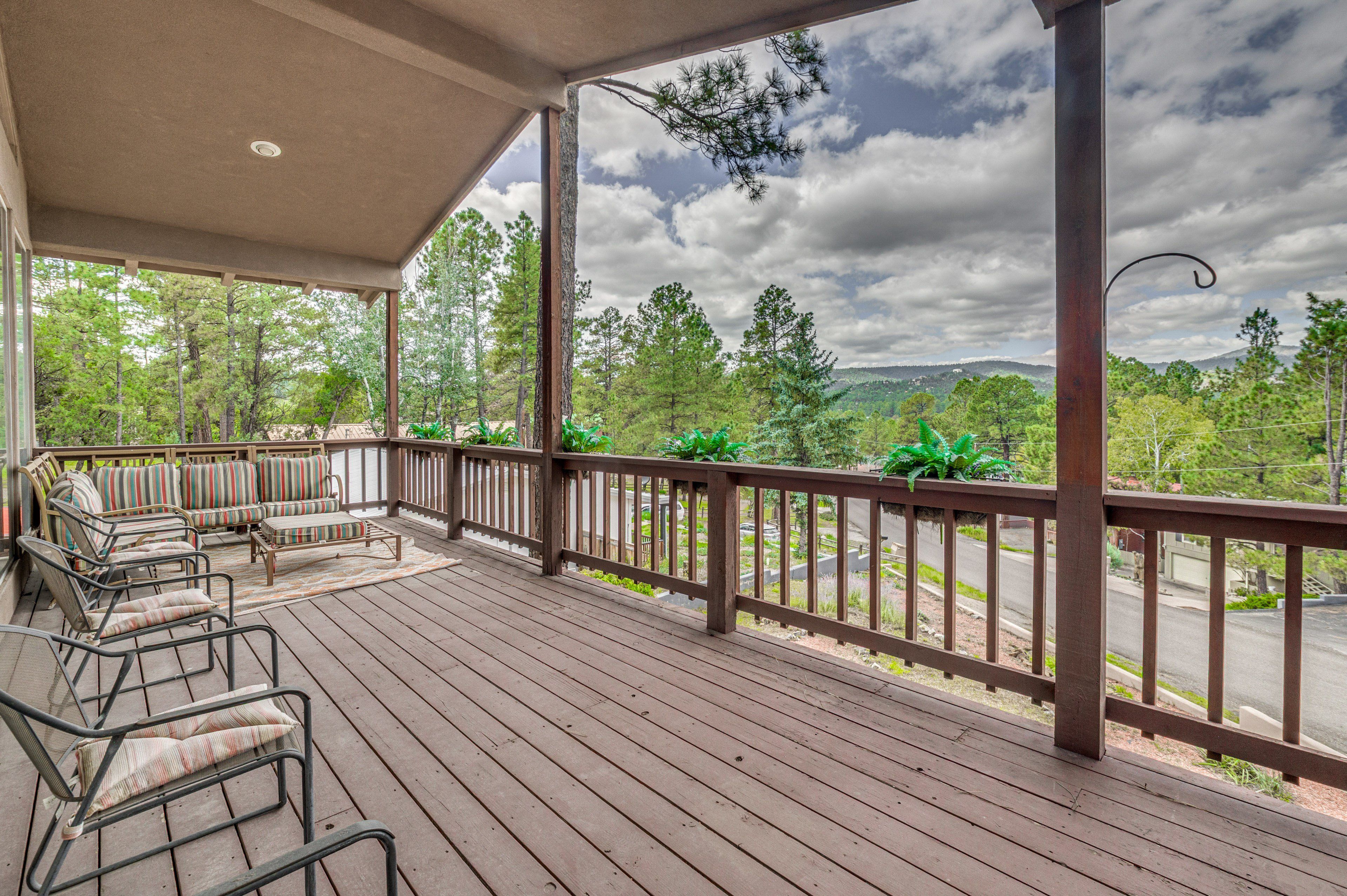 A covered outdoor deck with wooden flooring, metal chairs, and a sofa.