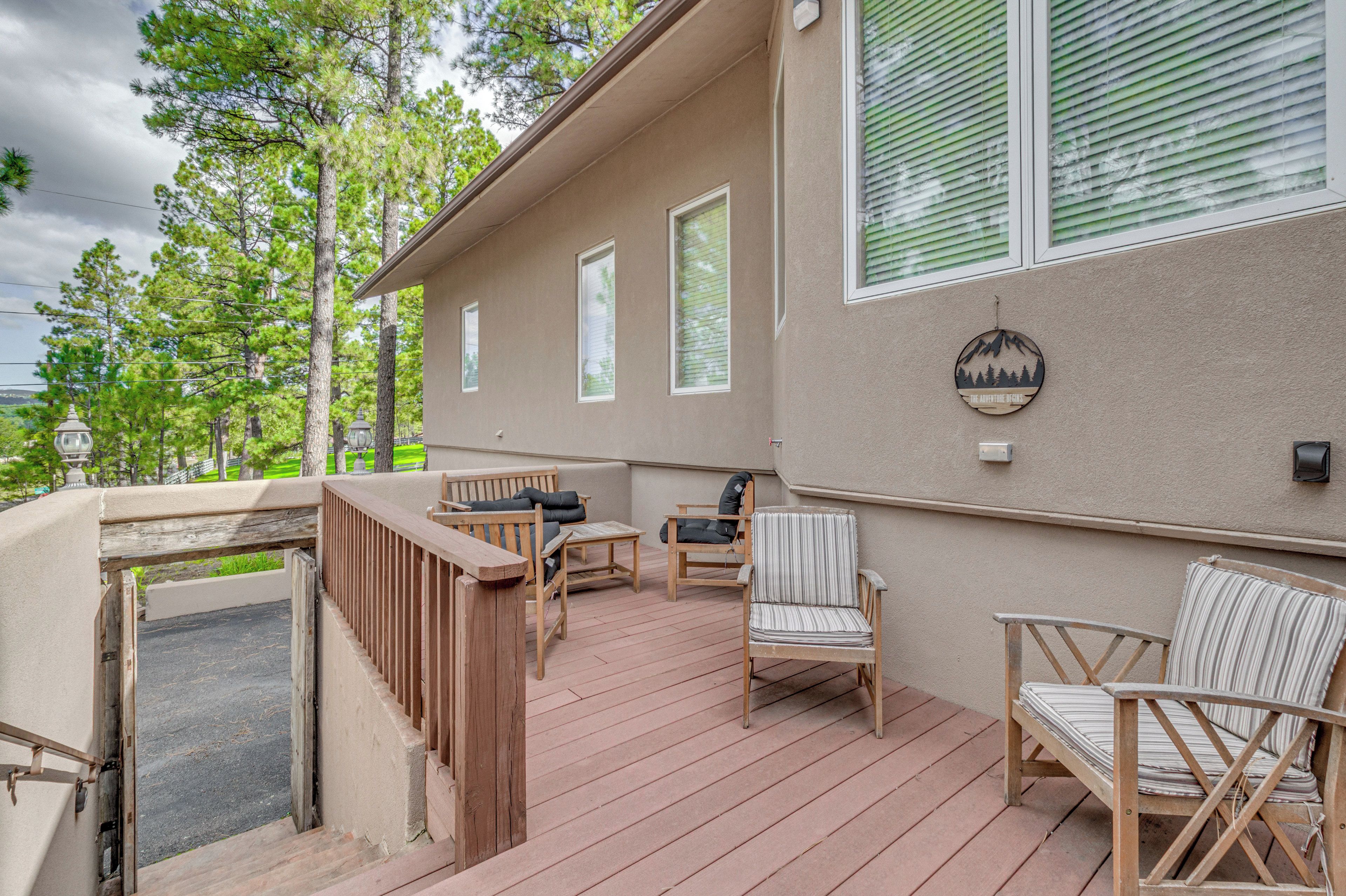 A covered outdoor deck with wooden furniture, including chairs and a table, and a view of a forested area.