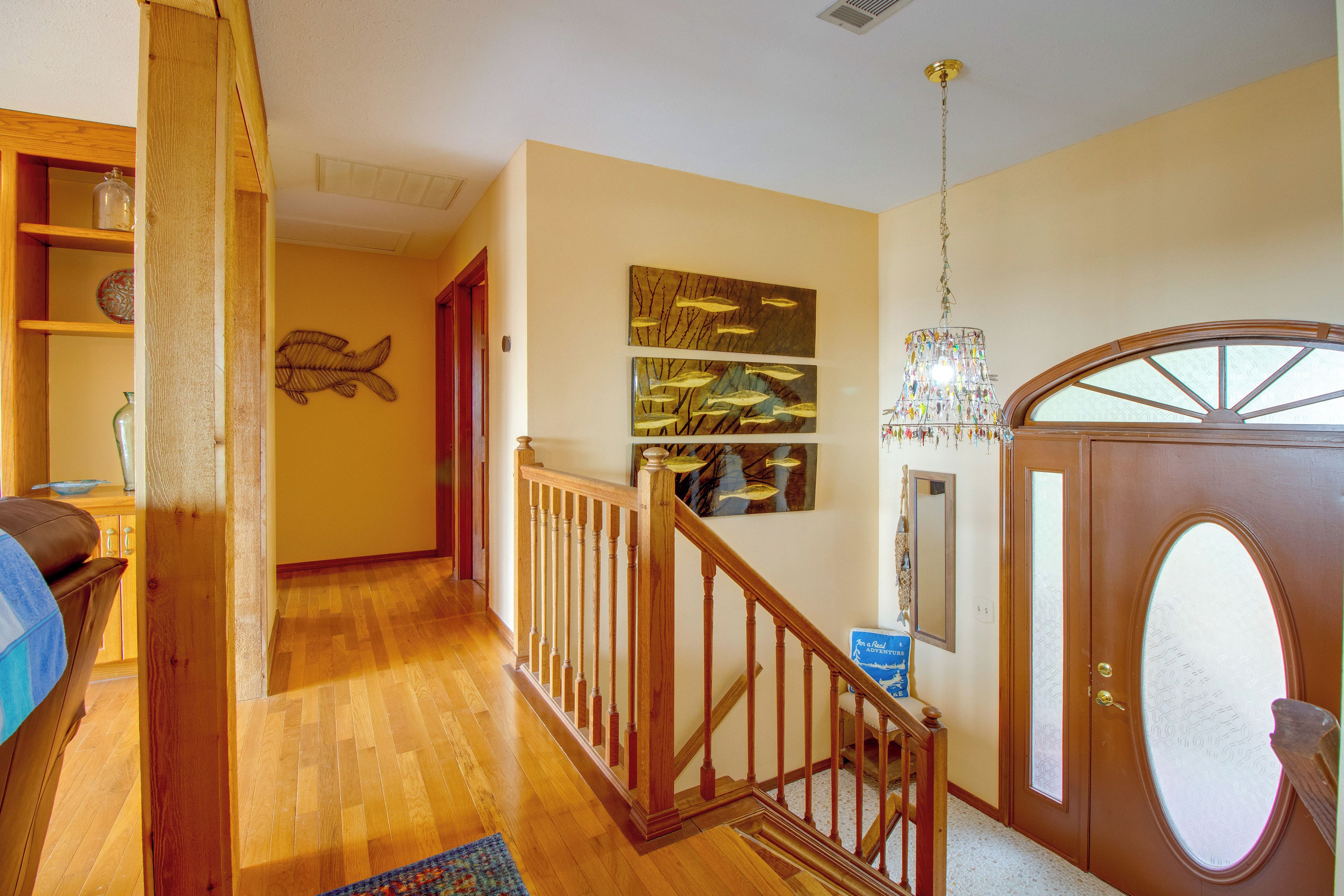 A wooden staircase leading to a landing with a chandelier and artwork on the wall.
