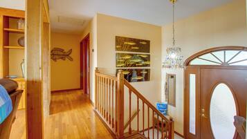 A wooden staircase leading to a landing with a chandelier and artwork on the wall.