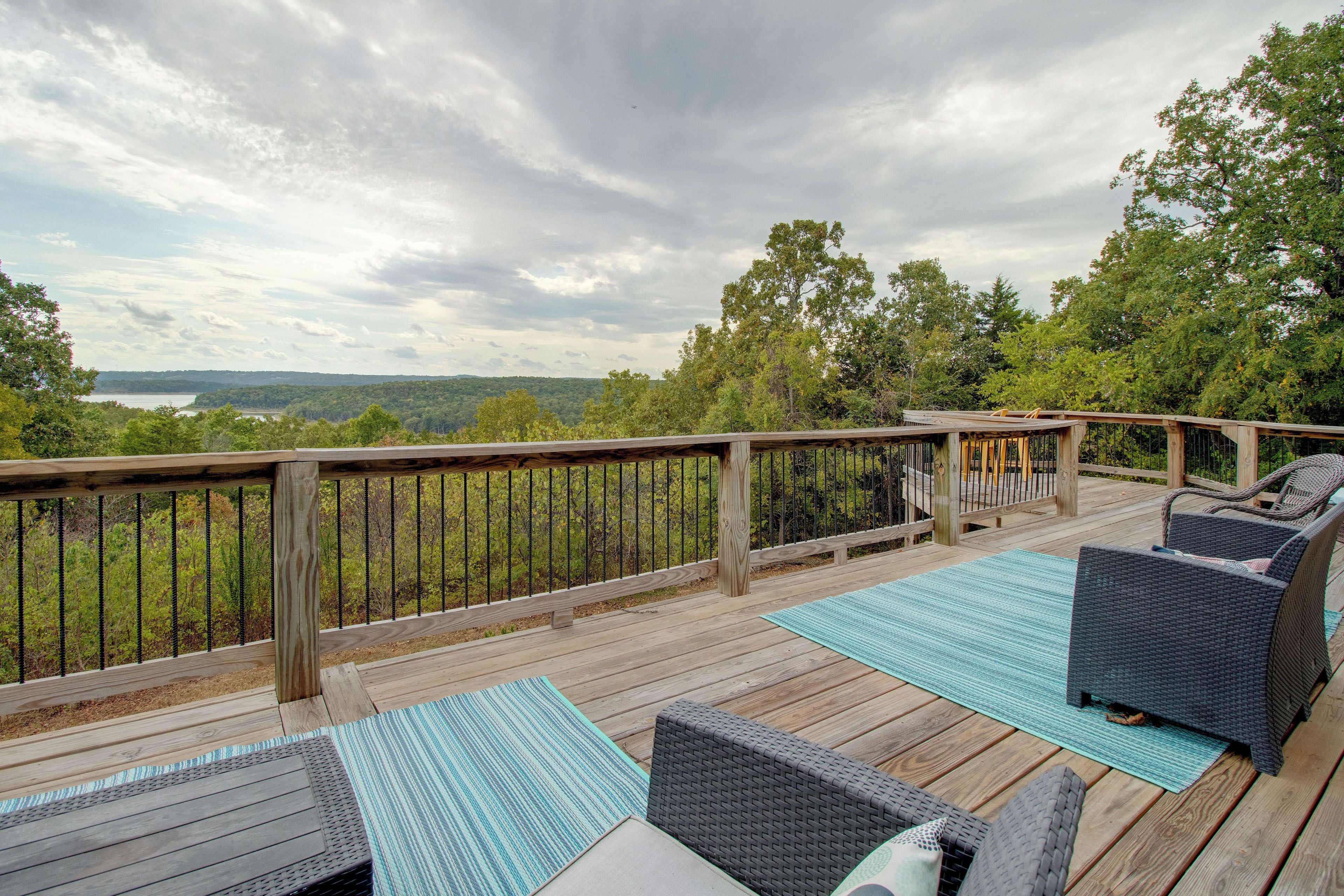 A wooden deck with outdoor furniture and a railing overlooking a forested landscape.