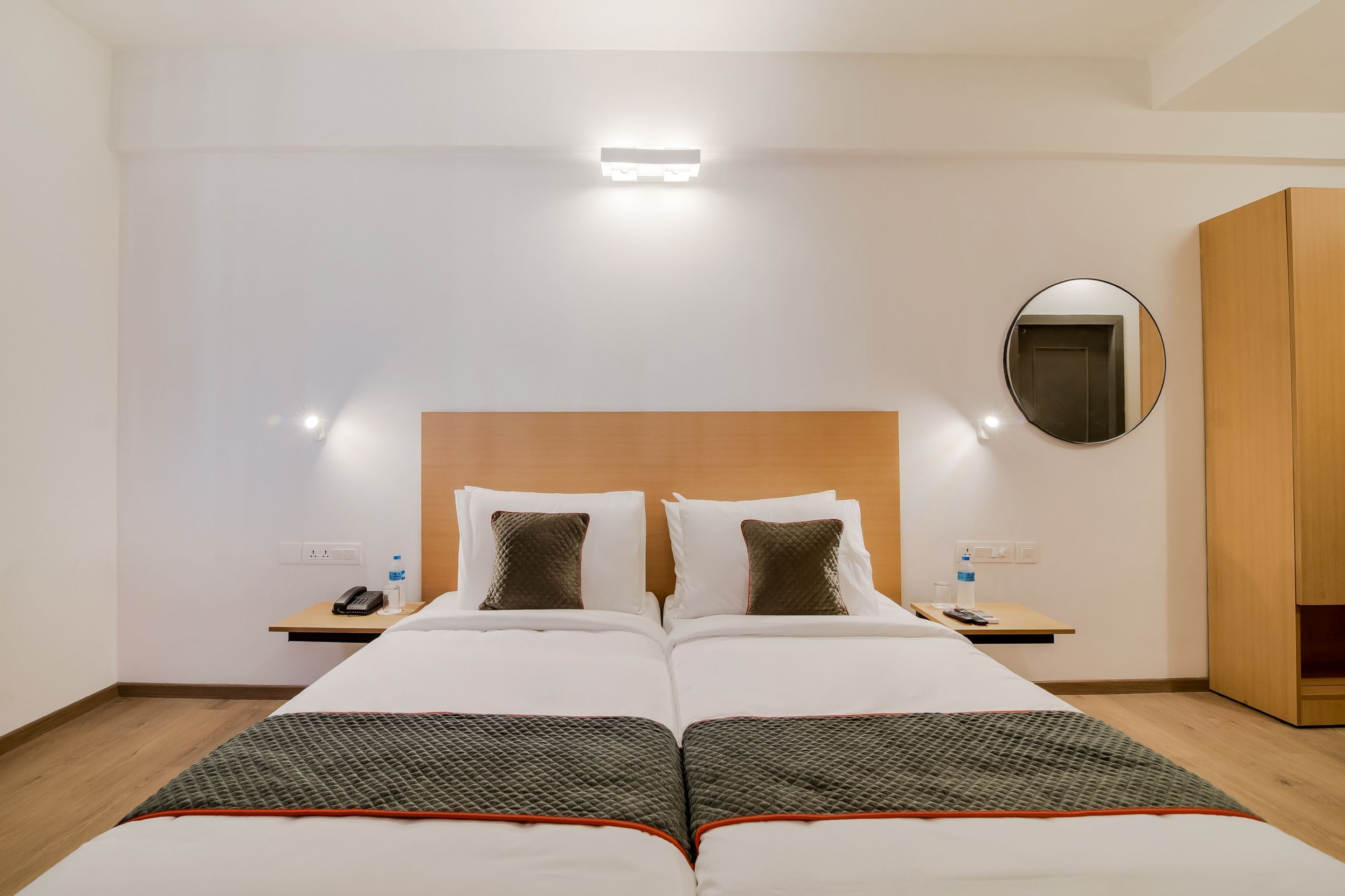 Una habitación de hotel con una cama doble, una mesita de noche con un teléfono y una botella, un espejo y un armario.