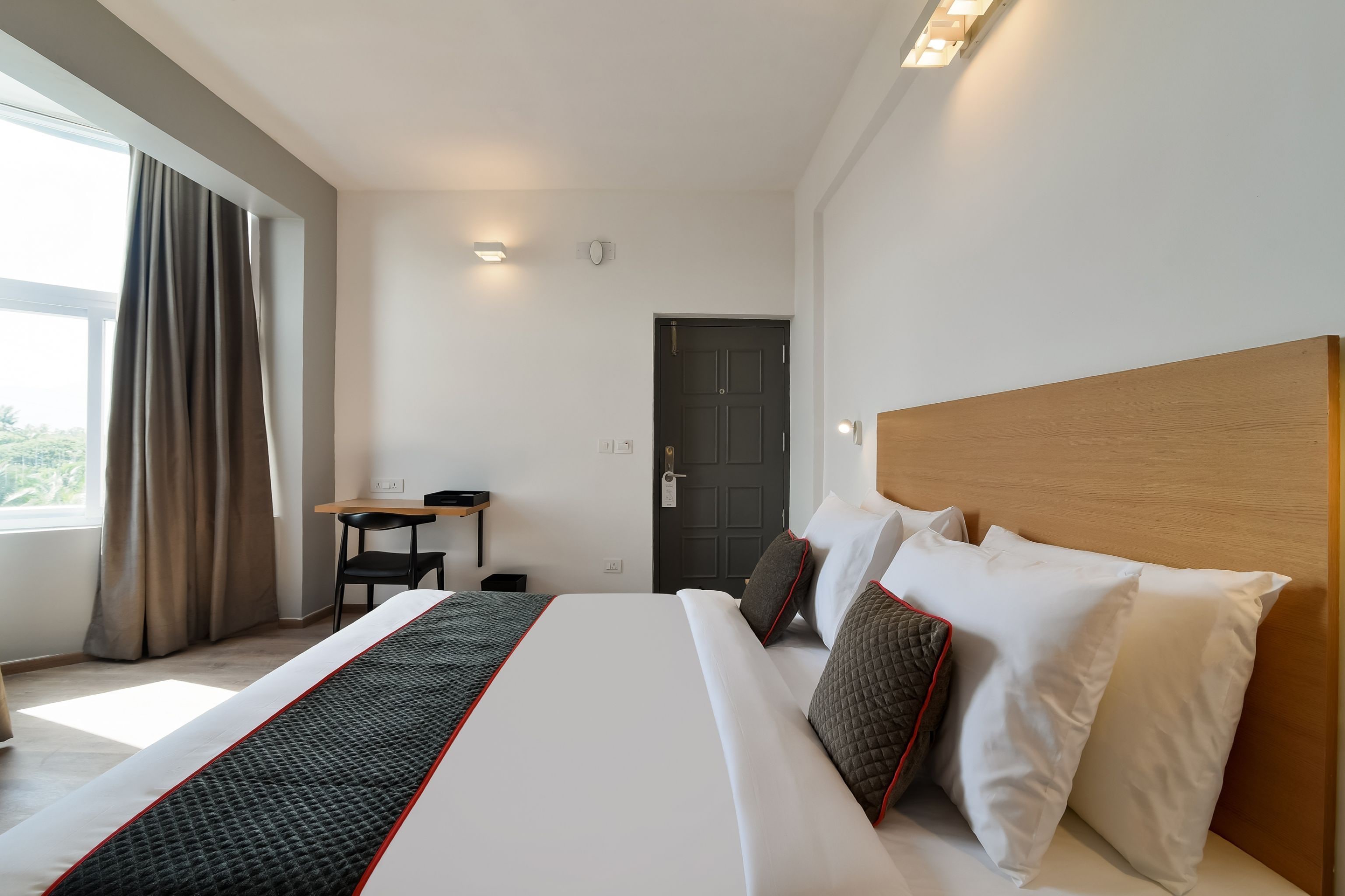 A hotel room with a large bed, a desk, and a view through a window.
