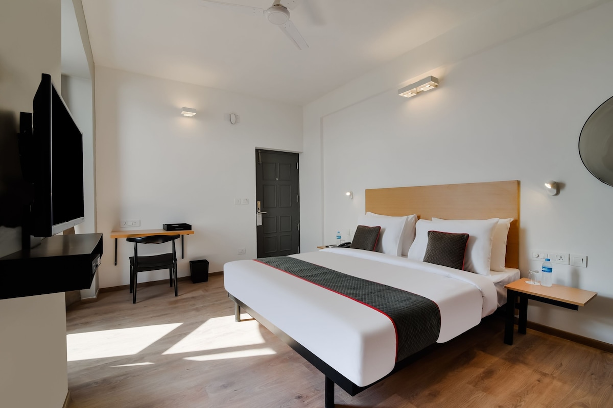 A hotel room with a bed, bedside tables, a desk, a chair, a TV, and a door.