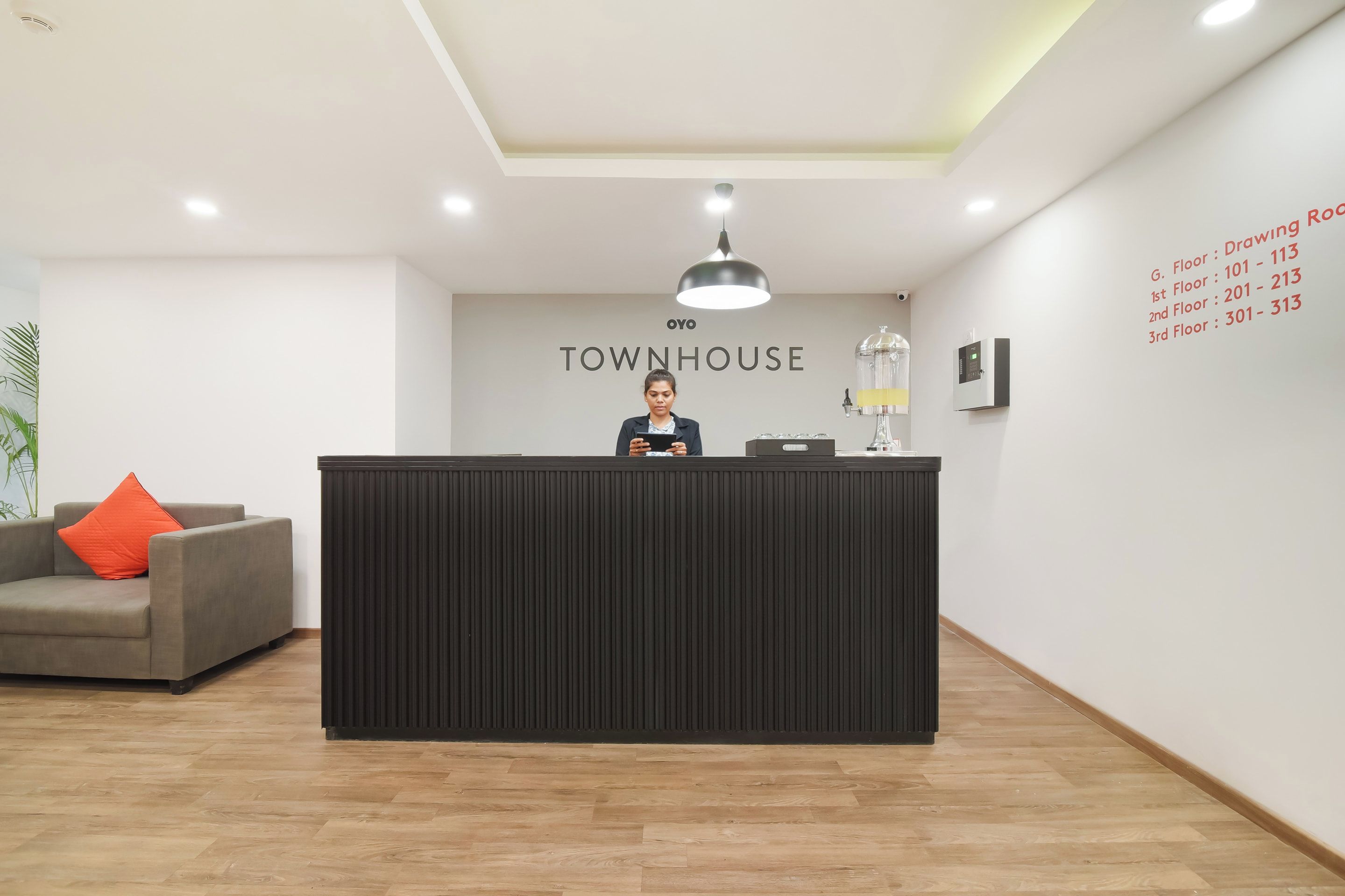 A reception desk with a modern design, a sign above it reading 'TOURHOUSE', and a wall with floor numbers and room numbers.