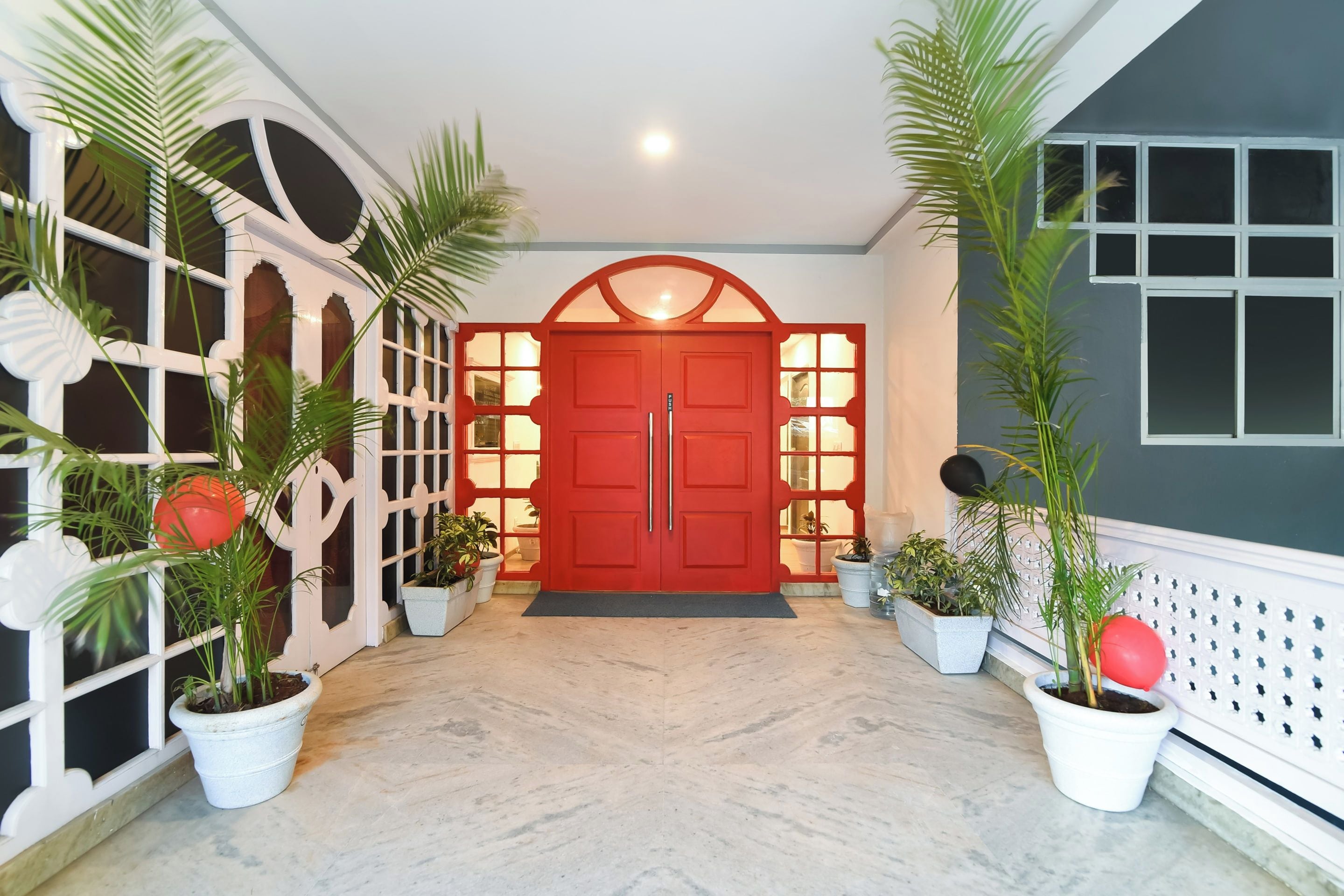 A hallway with a red door, potted plants, and a white railing.