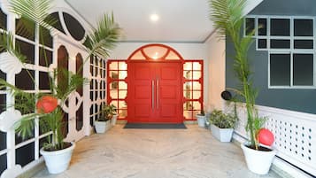 A hallway with a red door, potted plants, and a white railing.