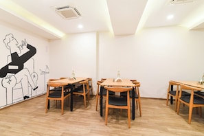 Un comedor con mesas y sillas de madera, un mural en la pared y una unidad de aire acondicionado en el techo.