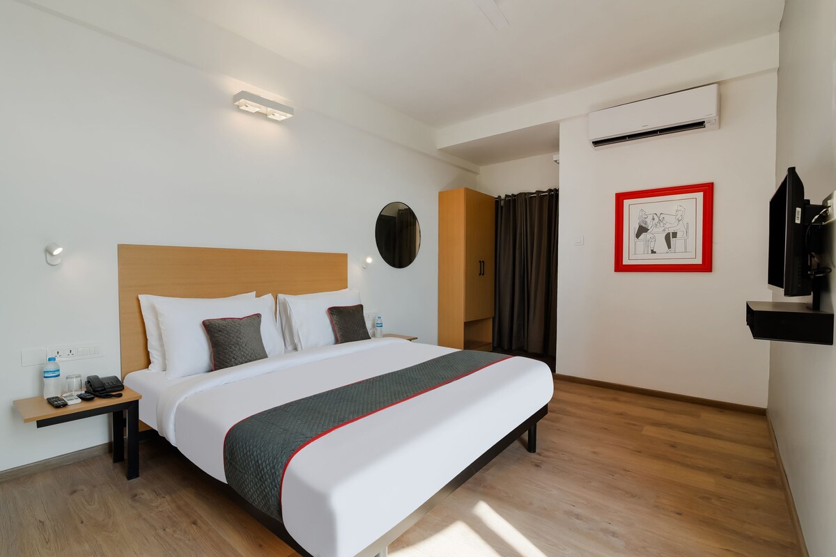 Une chambre d’hôtel avec un lit, une table de chevet, une bouteille d’eau, un téléphone et un tableau encadré au mur.