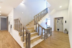 Una escalera de madera con tablones y barandillas, que conduce a un rellano con una puerta y una obra de arte colgada en la pared.