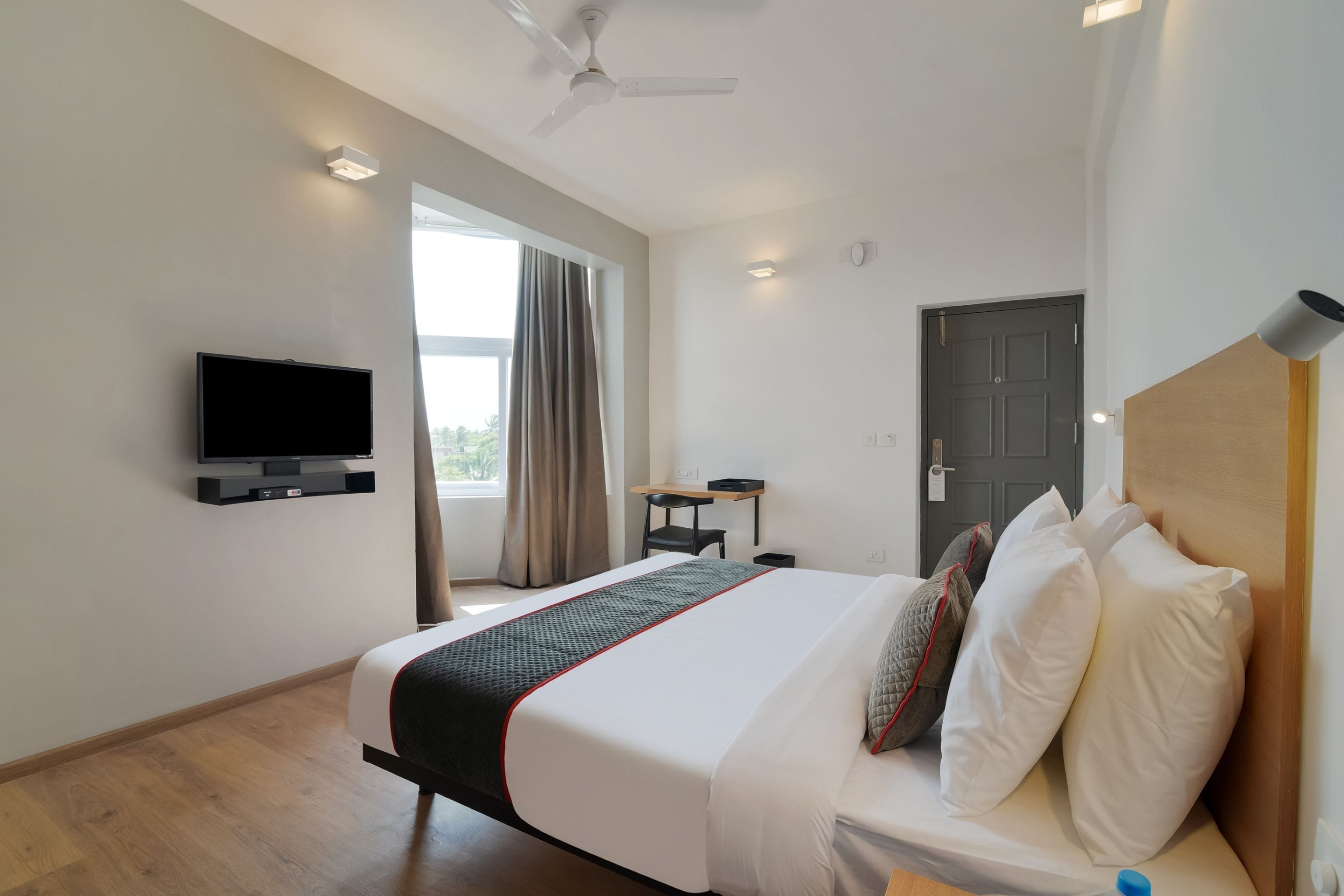 Una habitación de hotel con una cama, un escritorio, un televisor y una puerta.
