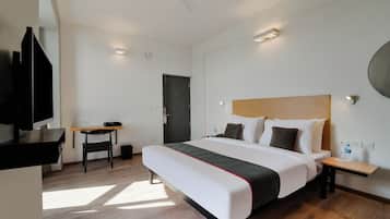 A hotel room with a bed, bedside table, chair, desk, and a TV.