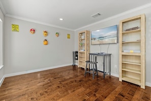 A room with wooden flooring, a television mounted on the wall, and a shelf unit with a 'WII' sign. - Home w/ Outdoor Entertainment Area in San Antonio! (San Antonio)