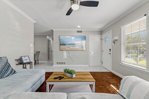 A modern living room with a ceiling fan, a mounted TV, and a view of the outdoors through a window. - Home w/ Outdoor Entertainment Area in San Antonio! (San Antonio)