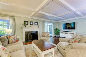 A spacious living room with a fireplace, comfortable seating, a television, and a large window.