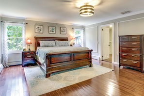 A bedroom with a wooden bed, bedside tables, a dresser, and a large window with curtains.