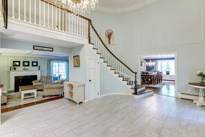 A spacious living room with a high ceiling, a staircase with a wooden handrail, and a dining area with a chandelier. - 3 Mi to Wadsworth Falls! Retreat w/ Backyard Oasis (Middletown)
