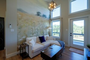 A living room with a white sofa, a dark coffee table, a painting on the wall, and a large window. - 1 Mi to Floyd Country Store: Cozy Mtn Cottage (Floyd)
