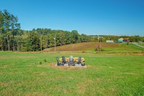 Un campo cubierto de césped con un pequeño espacio al aire libre que incluye sillas tipo Adirondack y una chimenea.