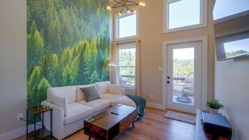 A modern living room with a white sofa, a wooden coffee table, and a forest mural on the wall.