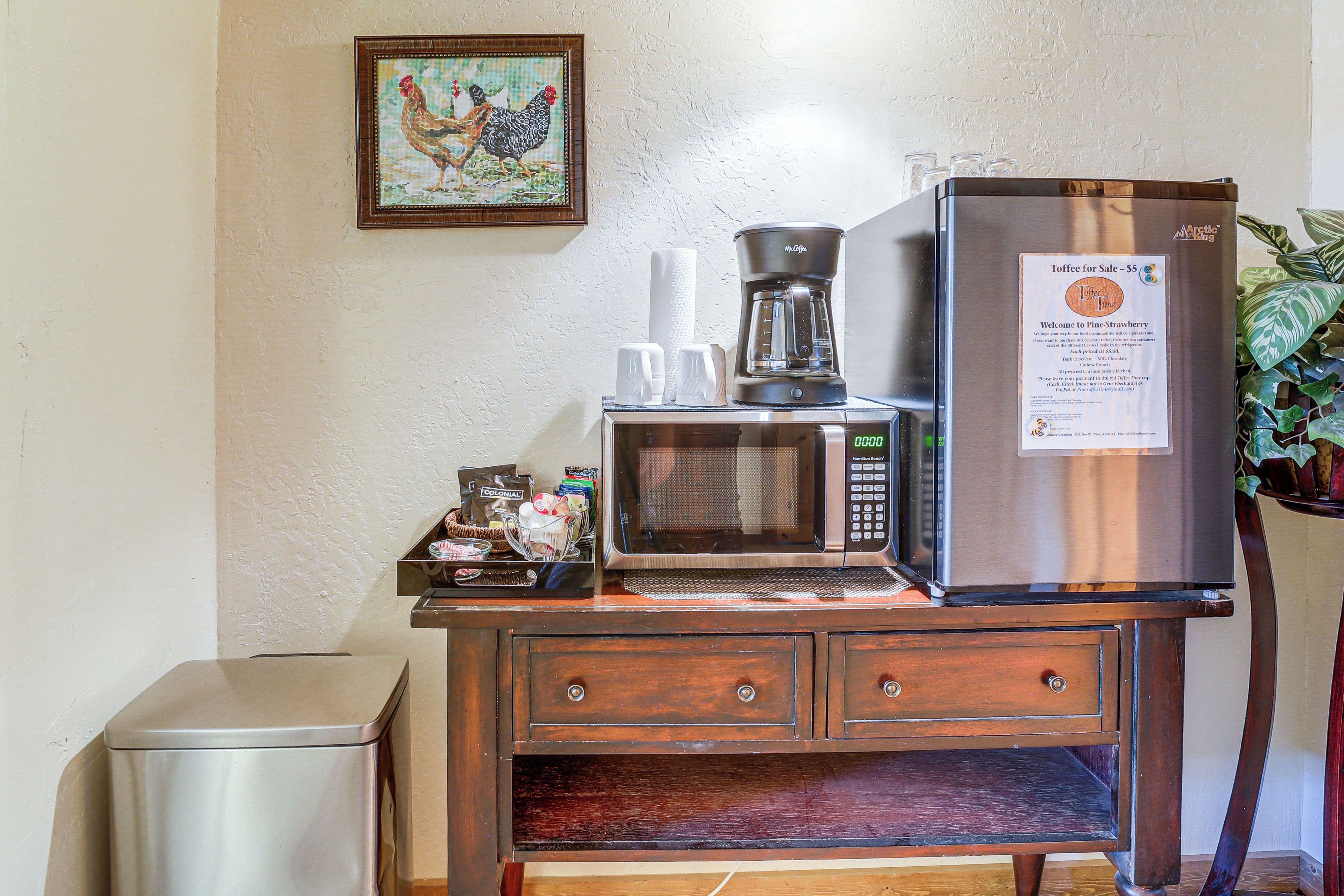 A kitchenette with a refrigerator, microwave, coffee maker, and a small trash bin.