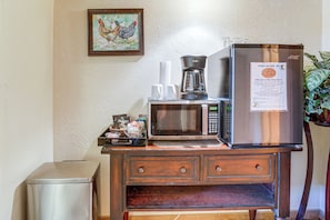 Una kitchenette equipada con refrigerador, microondas, cafetera y un pequeño bote de basura.