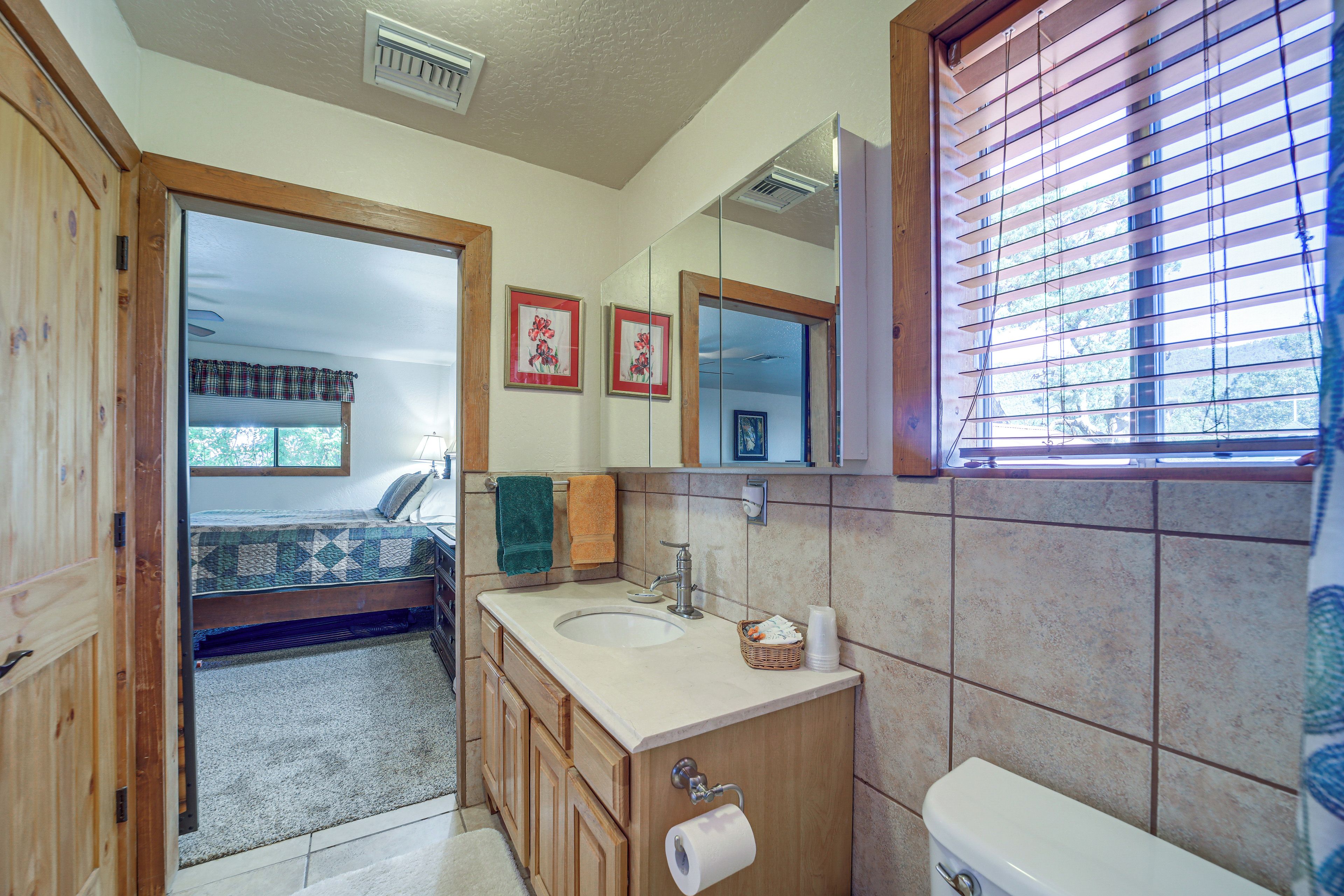 A bathroom with a wooden vanity, a toilet, a sink, and a window with blinds.