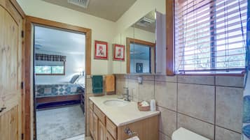 A bathroom with a wooden vanity, a toilet, a sink, and a window with blinds.