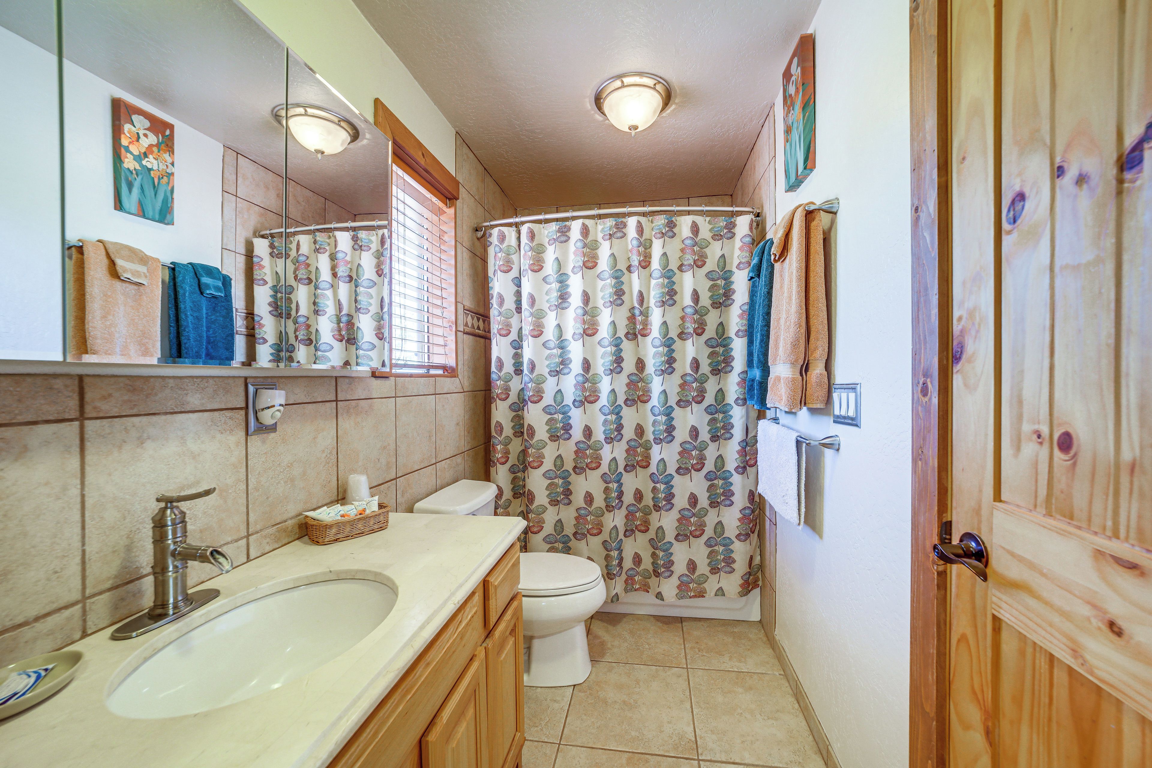 Baño con lavamanos, inodoro y cortina de ducha estampada con hojas.