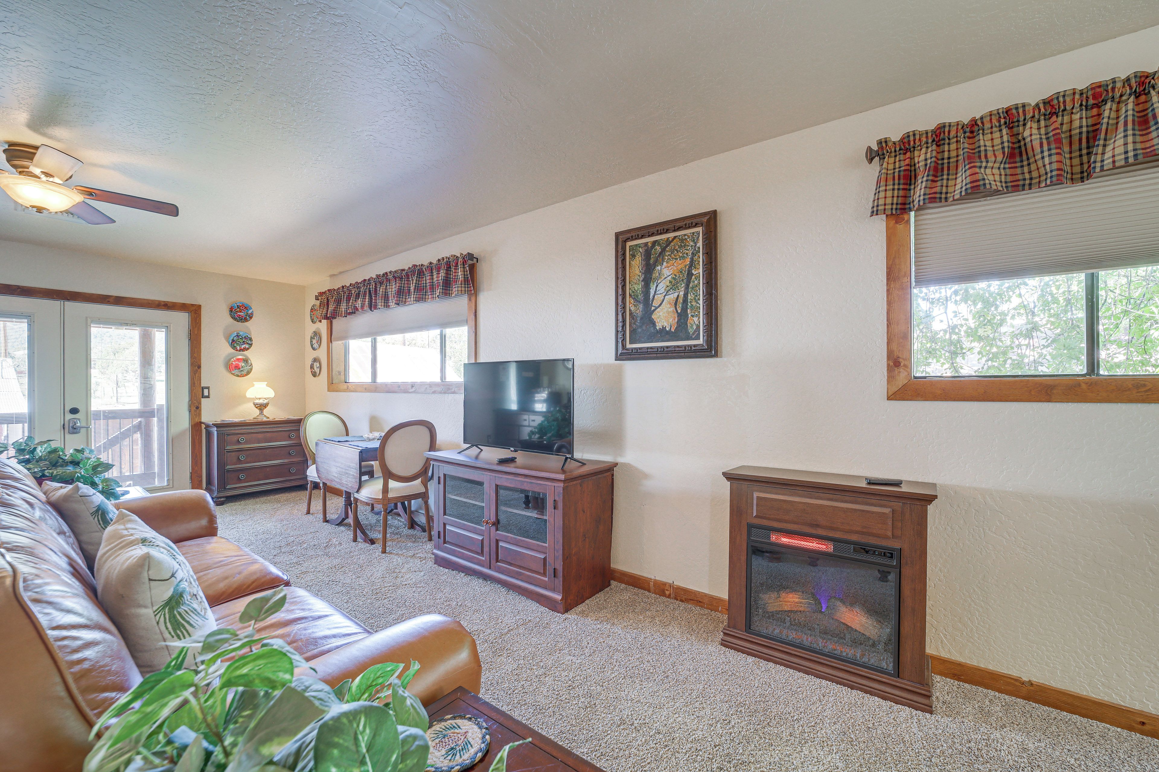 A living room with a fireplace, a television, a sofa, a dining table, and a ceiling fan.