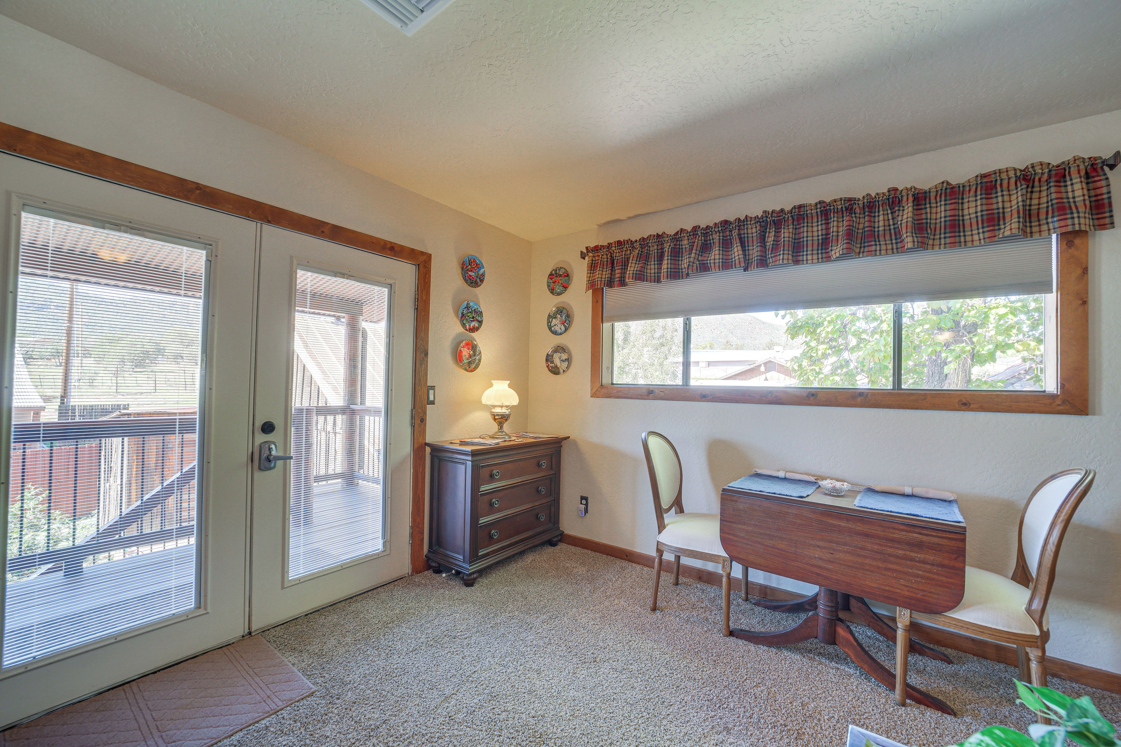 A room with a dining table, chairs, a lamp, a window with a plaid valance, and a door with blinds.