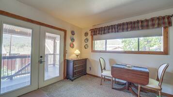 A room with a dining table, chairs, a lamp, a window with a plaid valance, and a door with blinds.