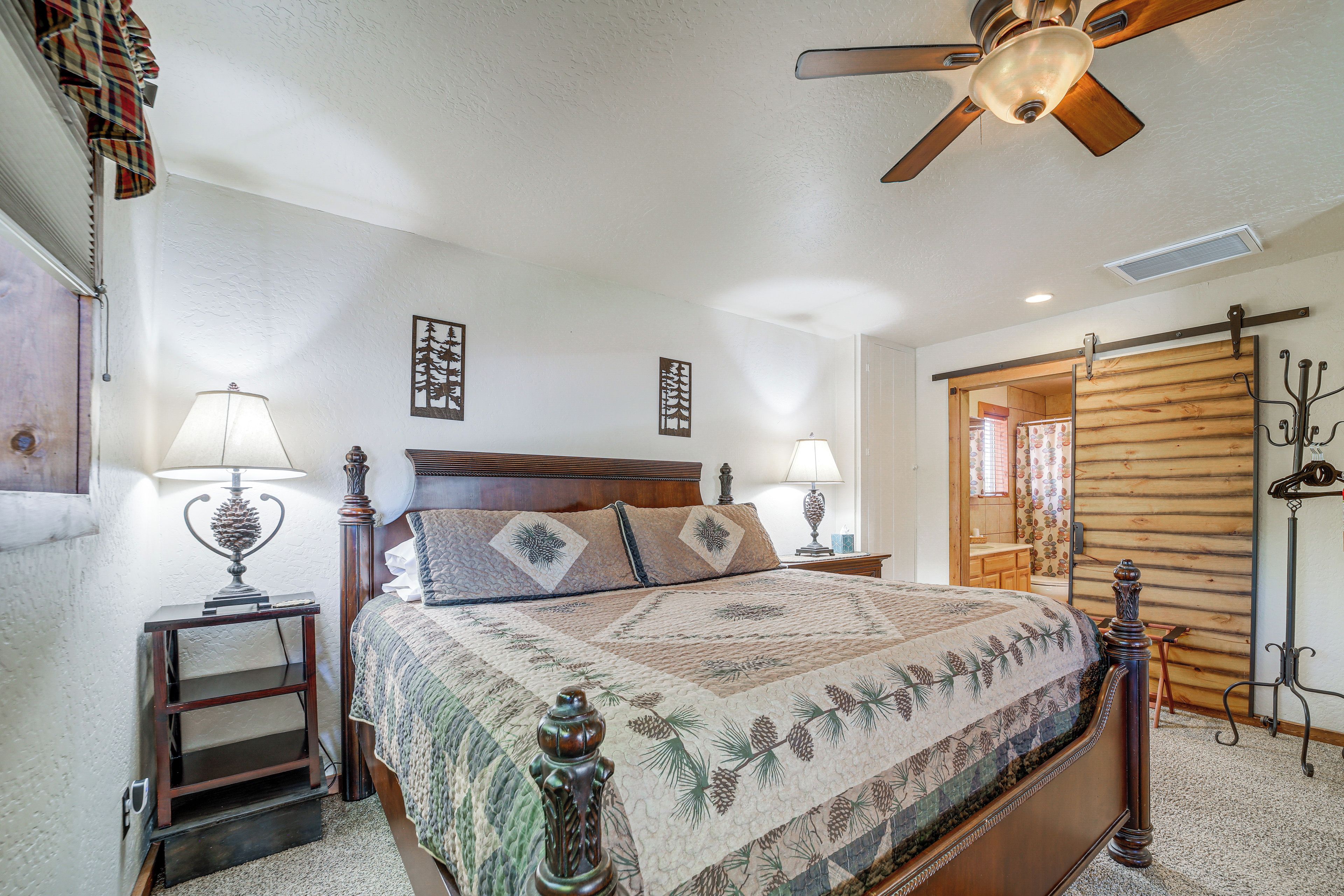 A bedroom with a bed, two bedside lamps, a ceiling fan, and a wooden door.