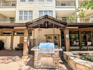 An outdoor grill area with a stone base, a metal roof, and a view of a multi-story building in the background. - Mountain View | King Bed | Hot Tub (Keystone)