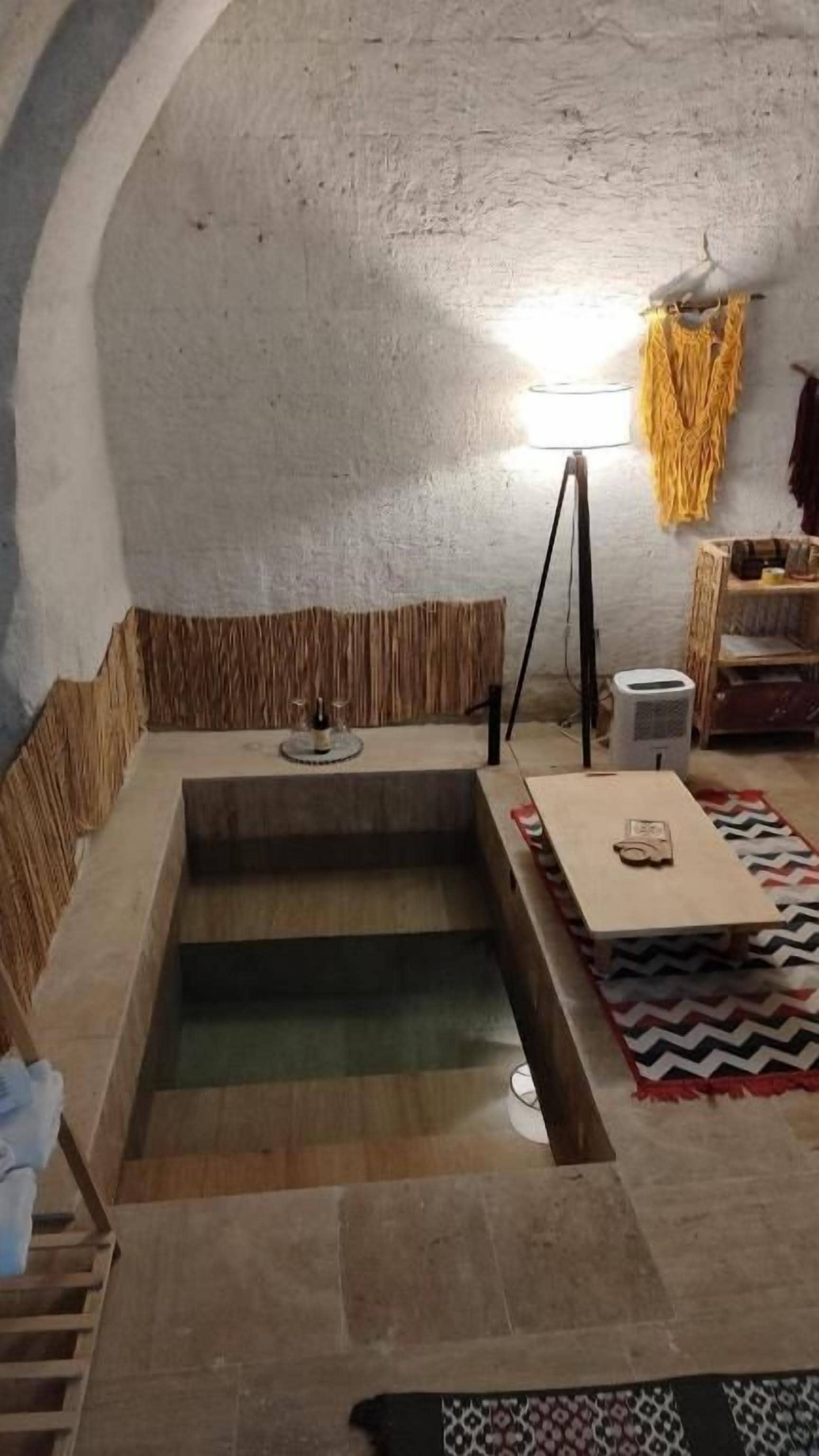 Ein Zimmer mit einer Steinbadewanne, einem Holztisch und einer Lampe.